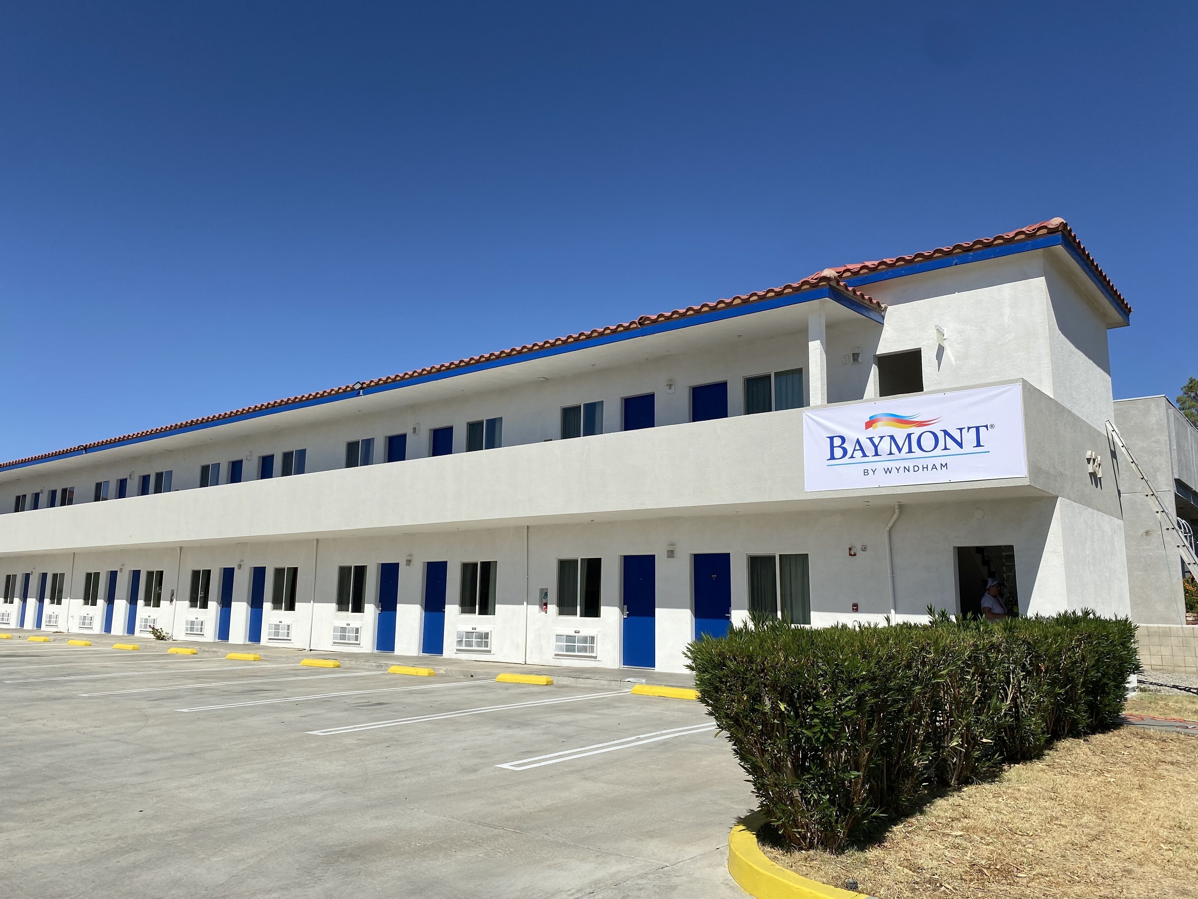 A Baymont hotel with a row of rooms, a parking lot, and a clear blue sky.