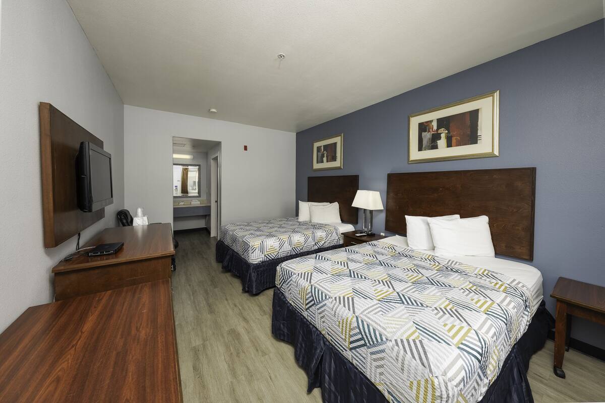 A hotel room with two beds, a desk, a TV, and artwork on the walls.