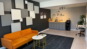 A modern living room with a sofa, a coffee table, a kitchen area with a sink and counter, and a wall with framed pictures.