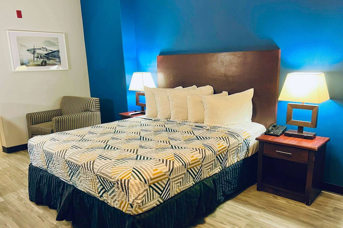 A hotel room with a large bed, two bedside tables with lamps, a chair, and a framed picture on the wall.