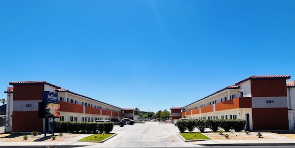 A hotel with a red and white facade, numbered 131, featuring a central courtyard with small plants and a clear blue sky.