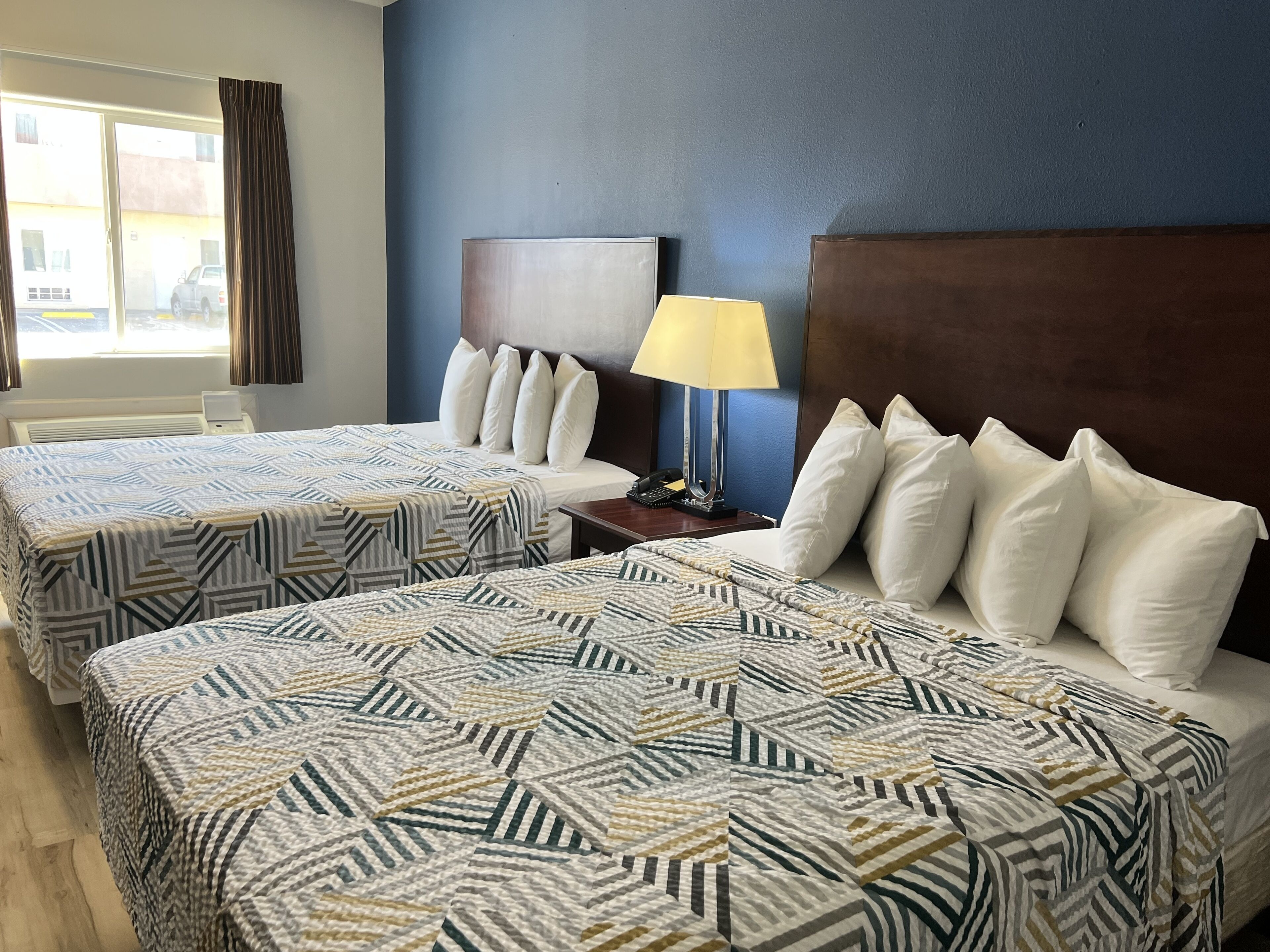 A hotel room with two beds, a nightstand, a lamp, and a window with curtains.