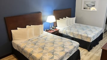 Quarto de hotel com duas camas, uma mesinha de cabeceira com abajur e um quadro na parede.