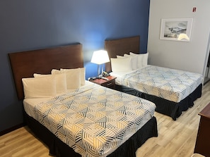 A hotel room with two beds, a nightstand with a lamp, and a framed picture on the wall.