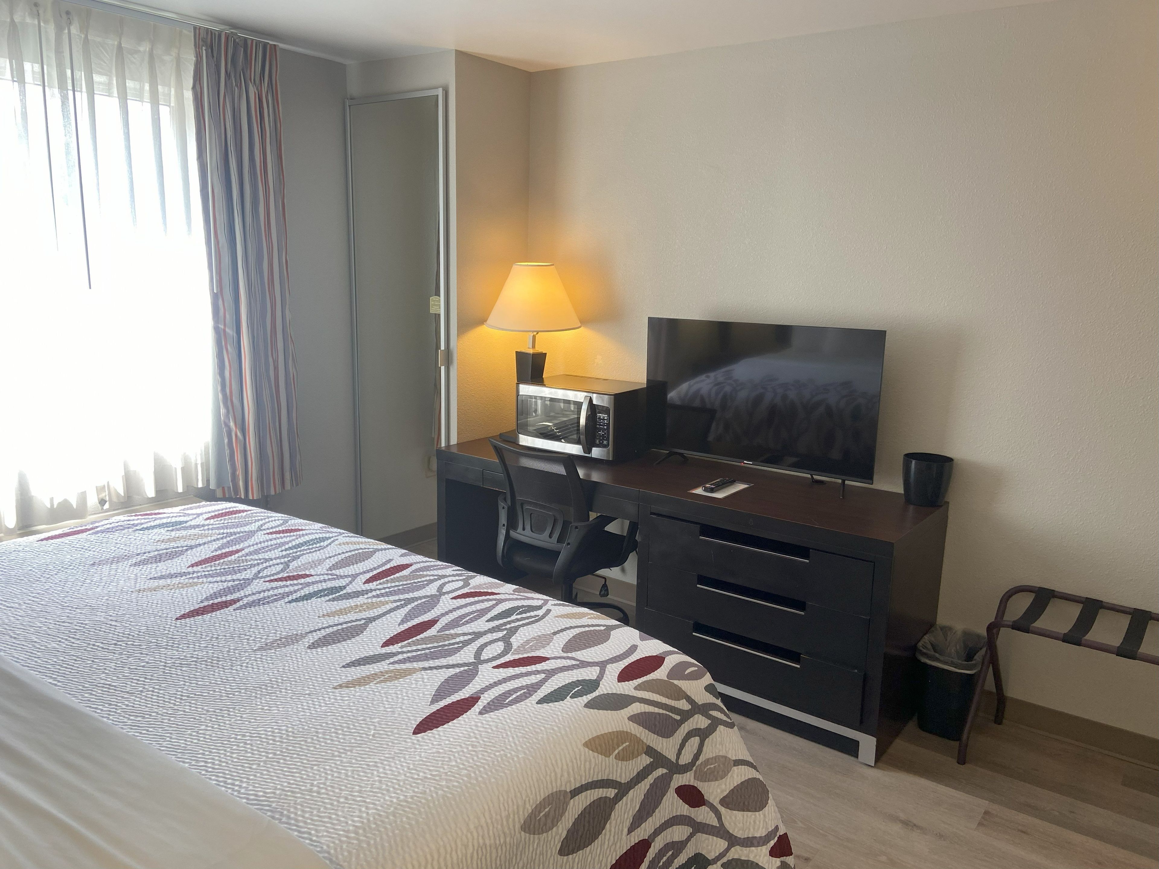 A hotel room with a bed, a desk with a TV, a lamp, and a chair.