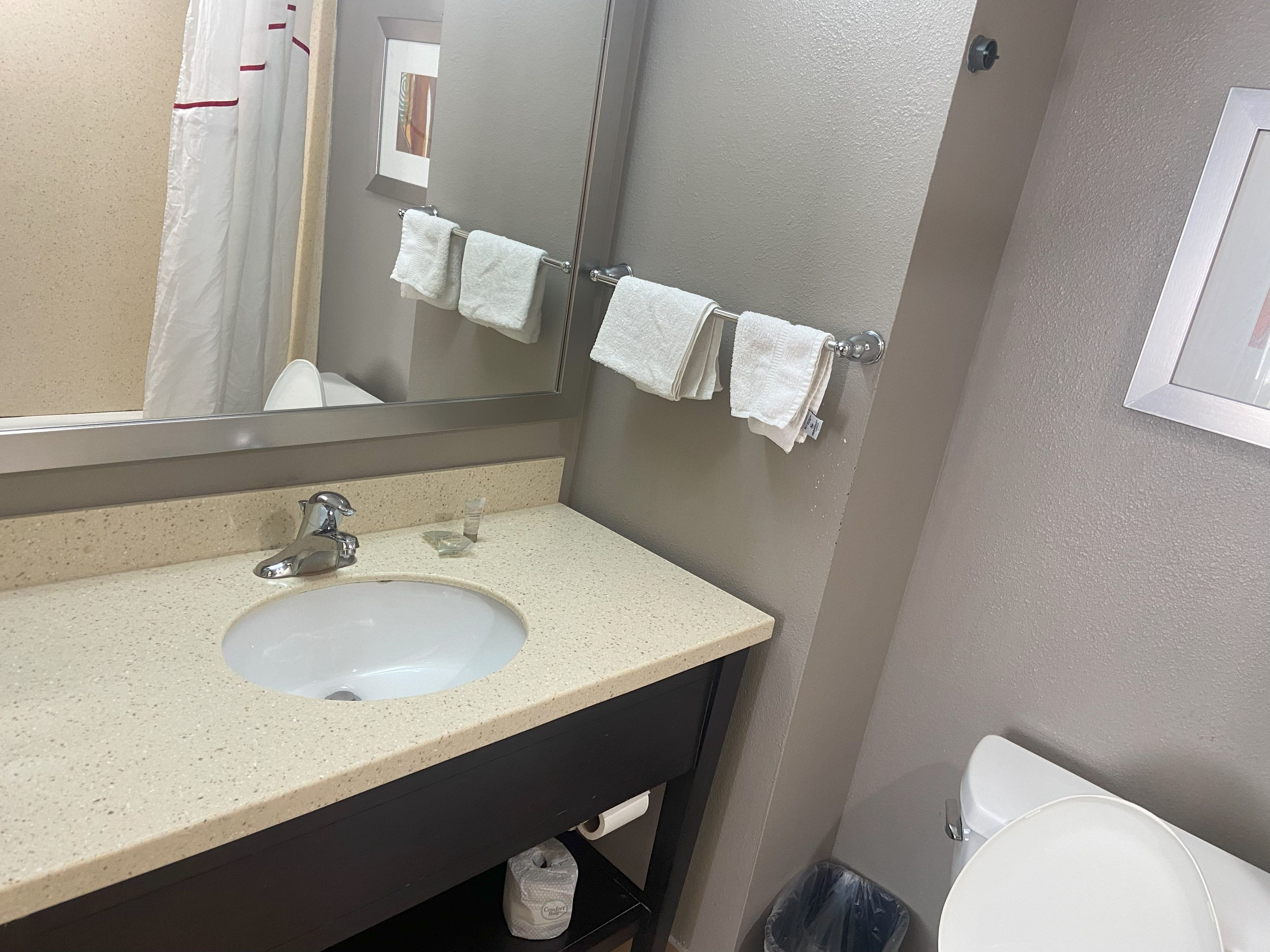 Un baño con lavamanos, espejo, toallero y retrete.
