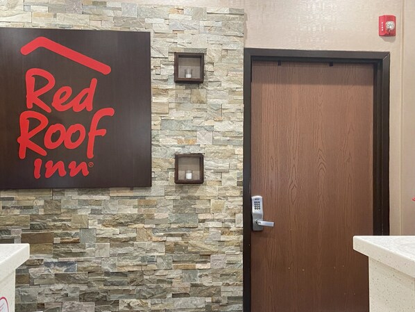 A Red Roof Inn sign on a stone wall, a wooden door, and a small shelf with a candle. - Red Roof Inn Pittsburgh - McKnight Rd (Pittsburgh)
