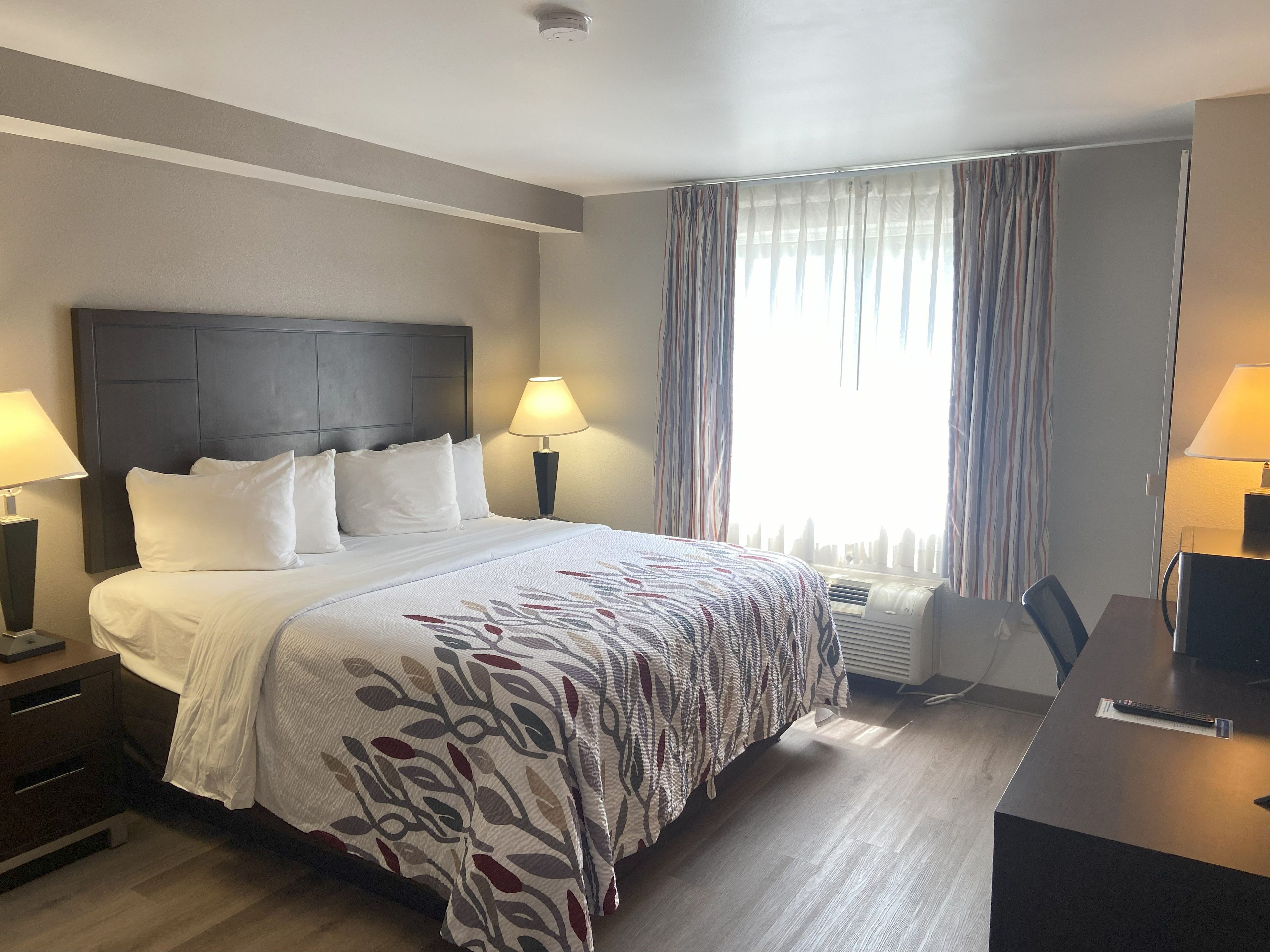 Habitación de hotel con una cama grande, dos mesitas de noche con lámparas, un escritorio con silla y una ventana con cortinas.