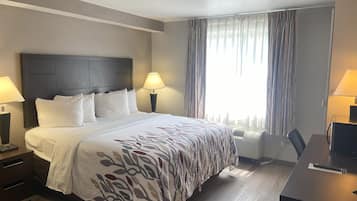 Habitación de hotel con una cama grande, dos mesitas de noche con lámparas, un escritorio con silla y una ventana con cortinas.