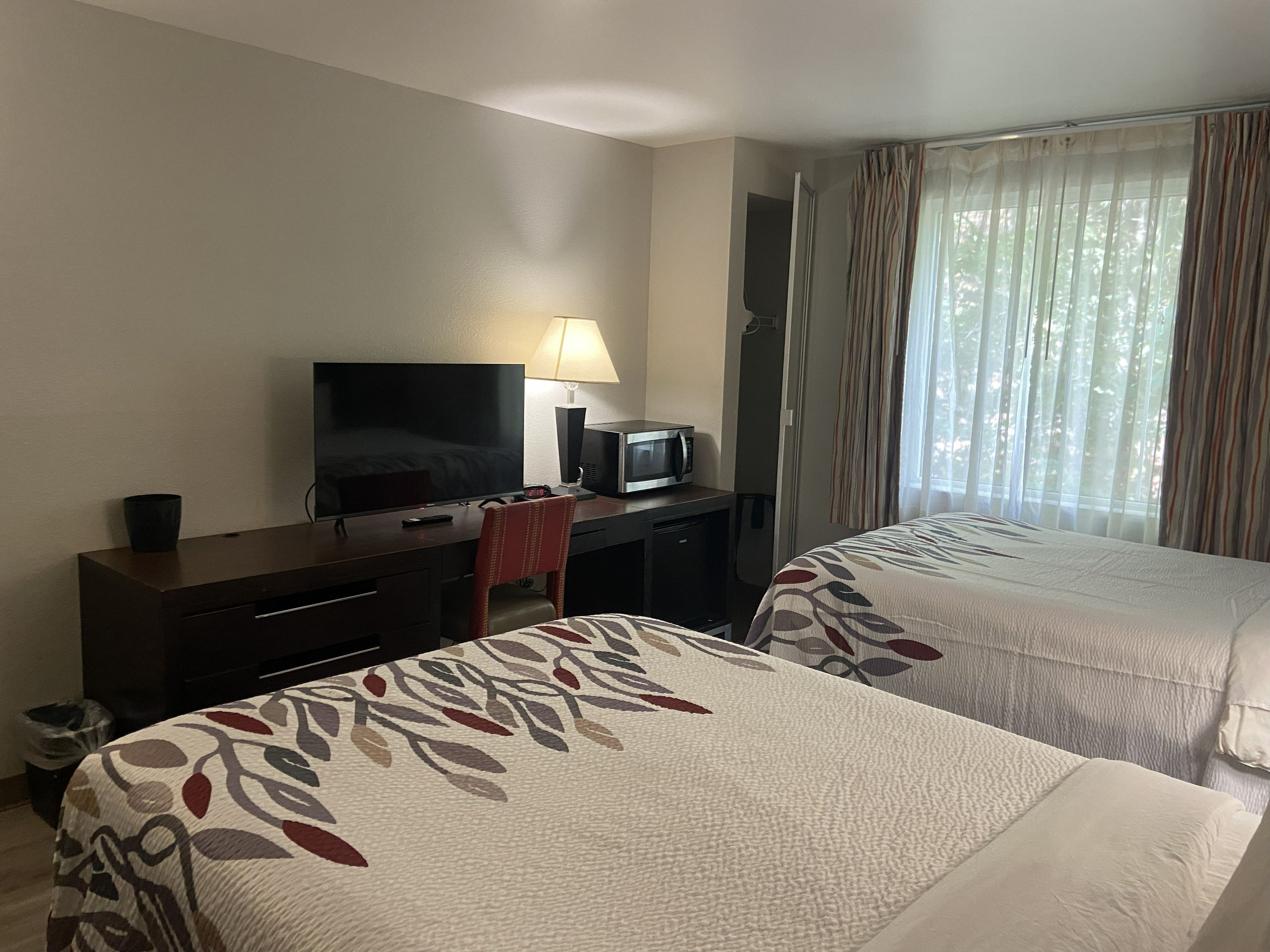 A hotel room with two beds, a desk with a television, a lamp, and a microwave.