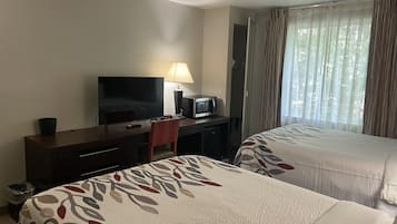 A hotel room with two beds, a desk with a television, a lamp, and a microwave.