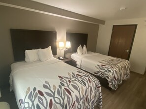 Une chambre d’hôtel avec deux lits, chacun recouvert d’une couvre-lit à motifs, une table de chevet avec une lampe et une porte.
