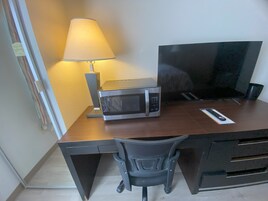 A compact workspace with a desk, a microwave, a lamp, a TV, and a chair.