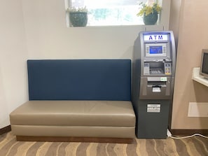 An ATM machine next to a blue cushioned bench in a room with a window and a plant. - Red Roof Inn Pittsburgh - McKnight Rd (Pittsburgh)