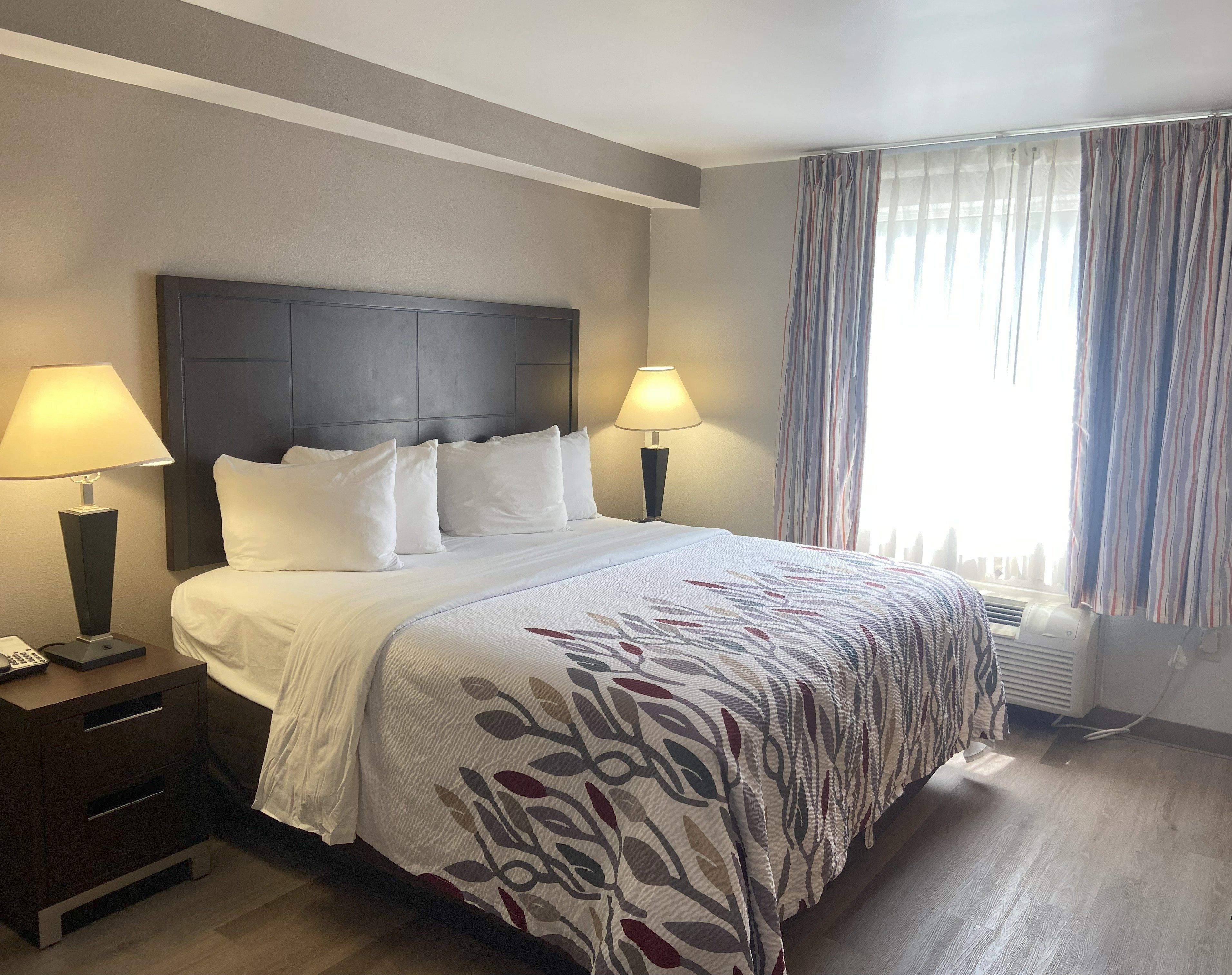 A hotel room with a large bed, two bedside lamps, a dark headboard, and a window with striped curtains.