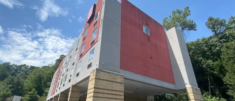 A multi-story building with a red facade and beige accents, featuring a parking area with several cars.
