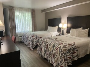 Hotellihuone, jossa on kaksi sänkyä, työpöytä ja tuoli.
