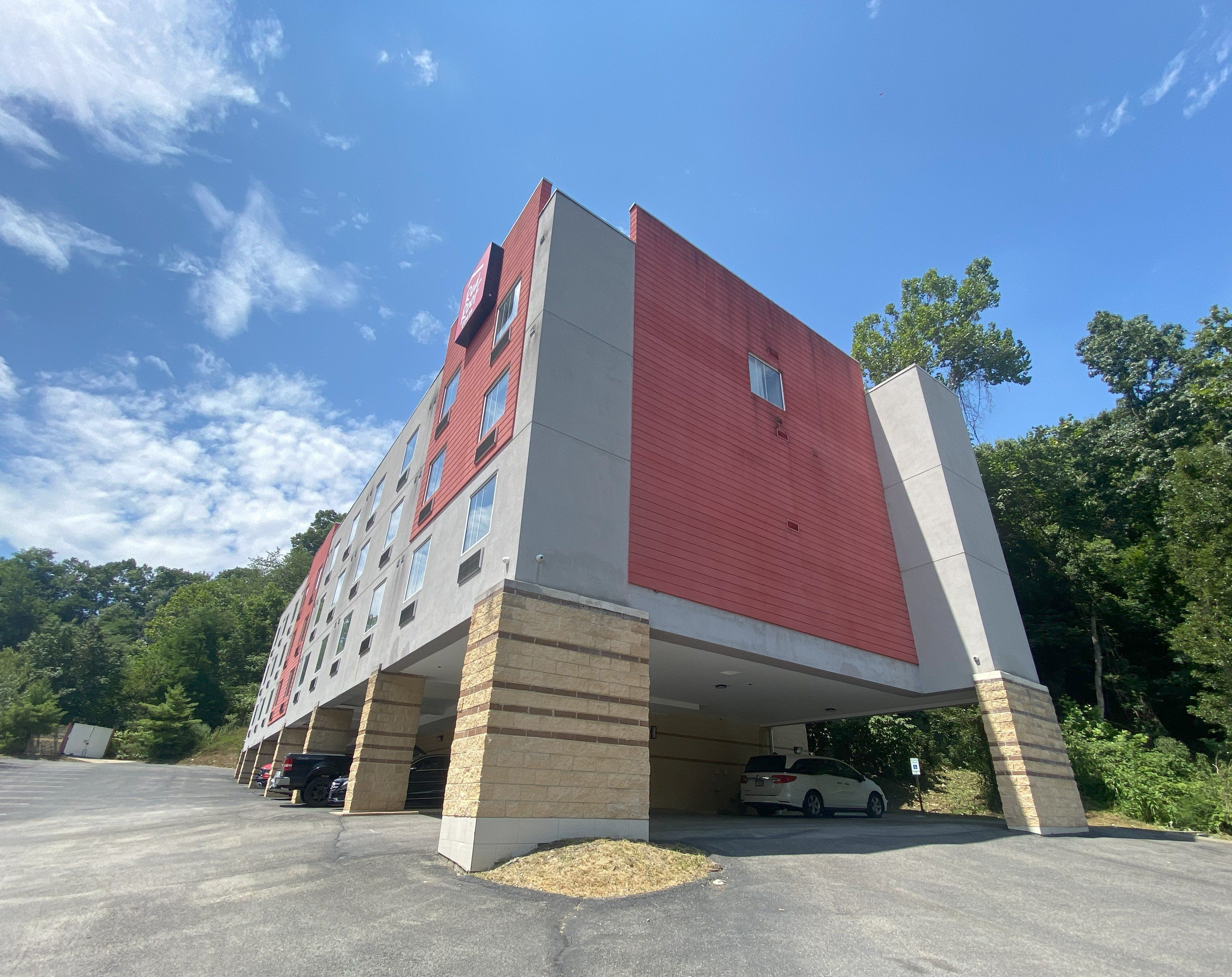 A multi-story building with a red facade and beige accents, featuring a parking area with several cars.