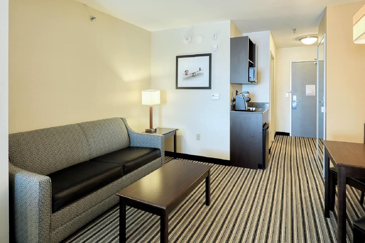 Ein Hotelzimmer mit einer Couch, einem kleinen Tisch, einer Lampe, einer Küchenzeile und einer Tür.