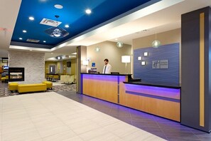 Un espace d’accueil d’hôtel au design moderne, comprenant un comptoir d’accueil, un coin salon et un logo bien visible sur le mur.