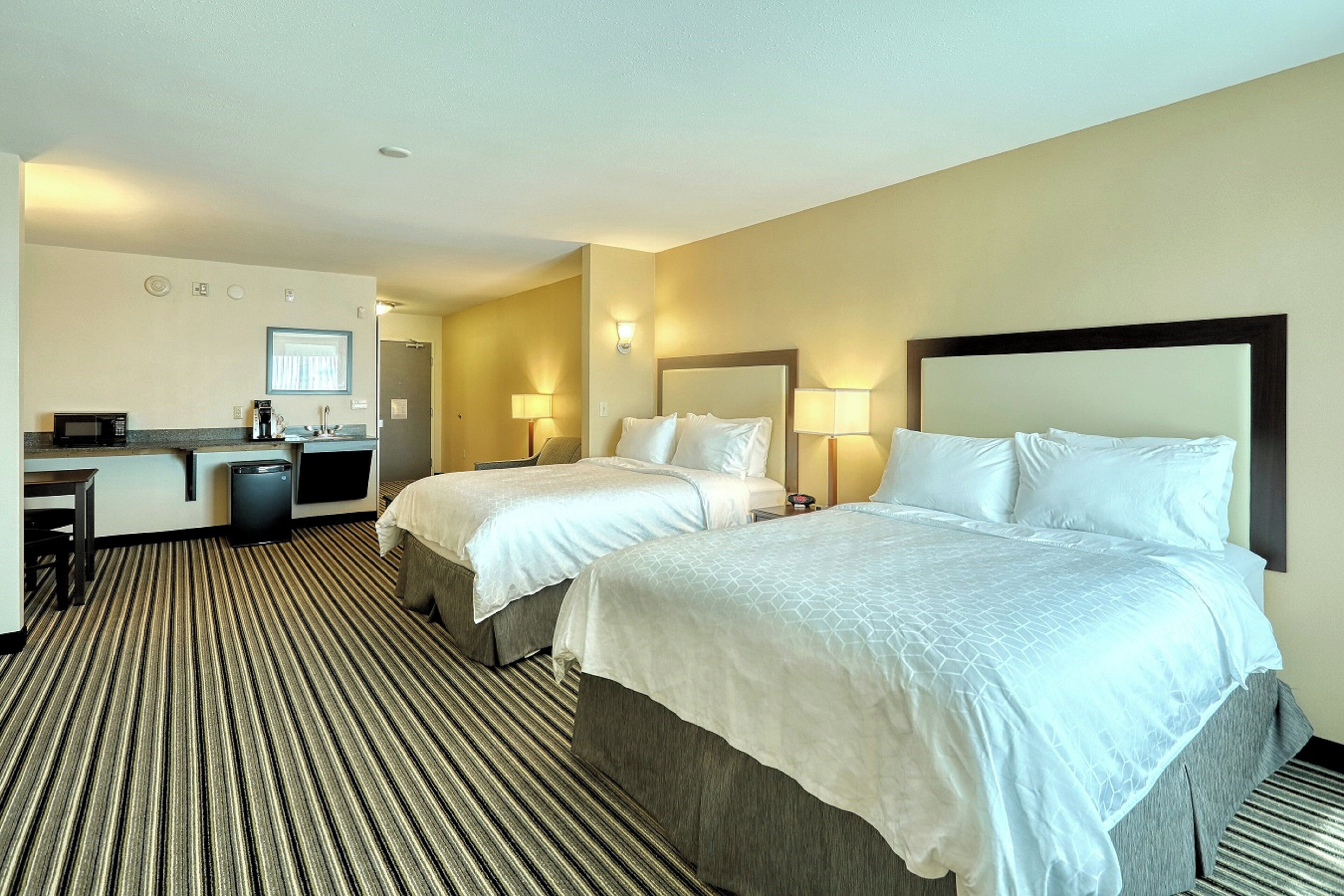 A hotel room with two beds, a desk, a microwave, and a small kitchenette.