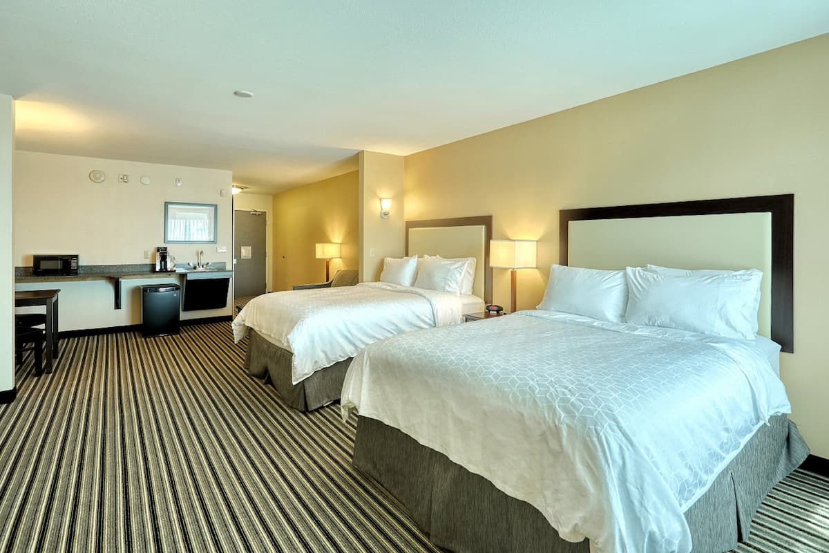 Ein Hotelzimmer mit zwei Betten, einem Schreibtisch mit Computer, einer Mikrowelle und einer kleinen Mülltonne.