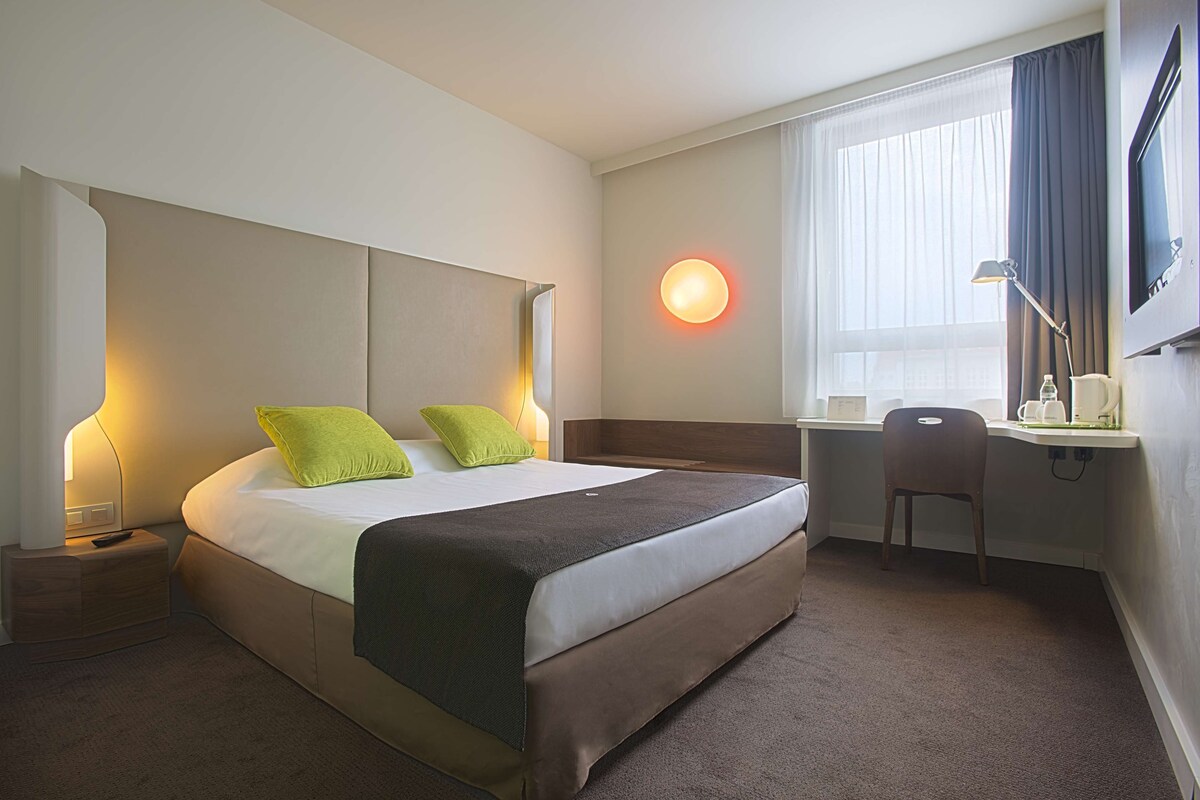 Una habitación de hotel con una cama grande, dos lámparas de noche, un escritorio y una silla.
