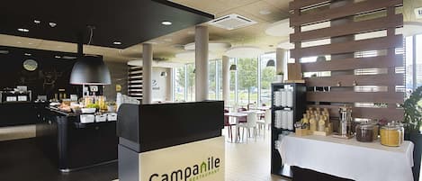 Interior de un restaurante de hotel con recepción, zona de buffet y mesas de comedor.