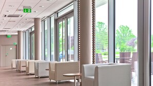 A modern waiting area with rows of chairs and tables, large windows, and an exit sign. - Campanile Wroclaw Centrum (Wroclaw)