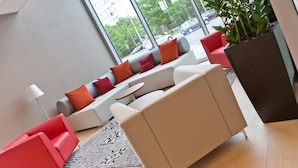 A modern lounge area with a sofa set, a red chair, a small table, and a large potted plant. - Campanile Wroclaw Centrum (Wroclaw)