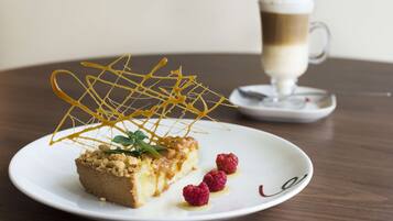 Un plato de postre con una porción de pastel, frambuesas y un hilo de caramelo sobre un plato blanco.