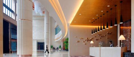 A spacious lobby with a reception desk, large columns, and a modern ceiling design.