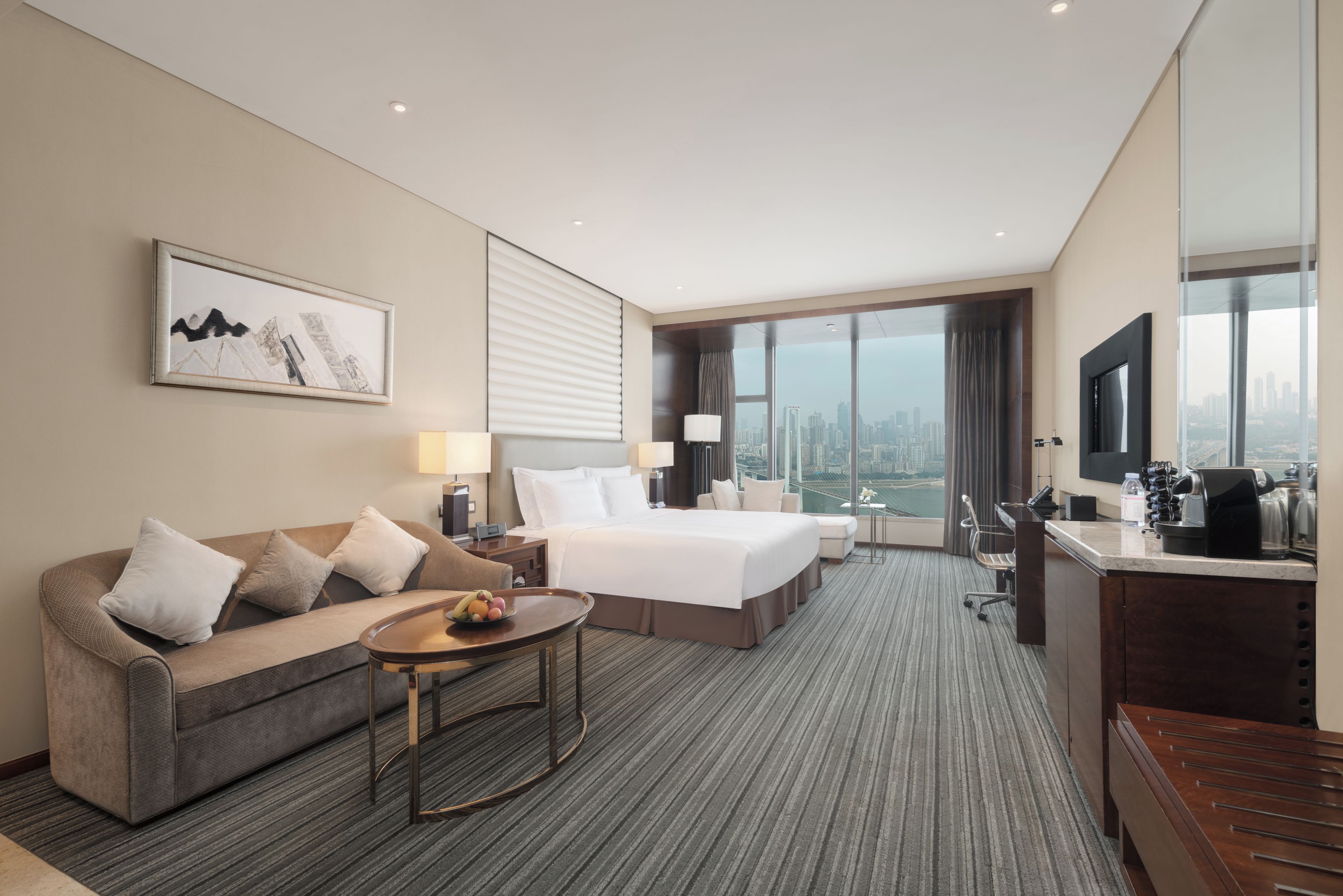Ein Hotelzimmer mit Bett, einer Couch, einem Schreibtisch und Blick auf die Stadt.
