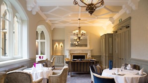 A dining area with round tables, chairs, a chandelier, and a fireplace. - Warren House (Kingston Upon Thames)