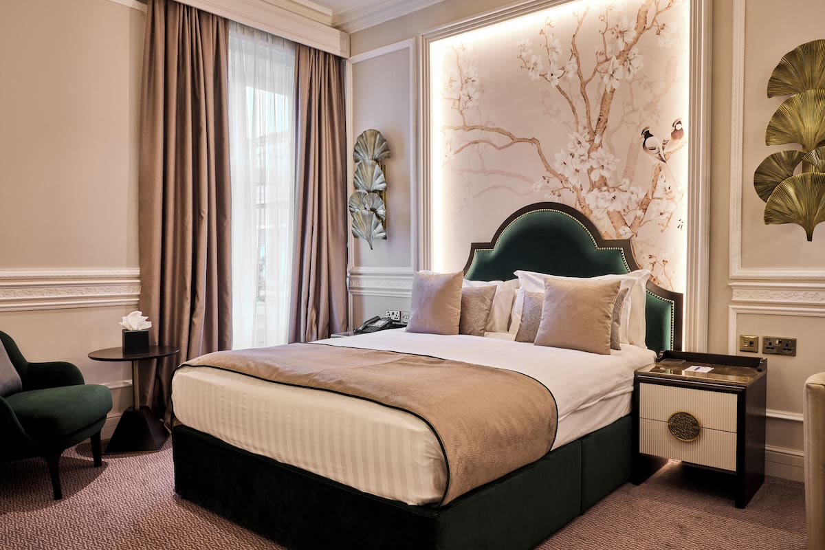 A hotel room with a large bed, a nightstand, a chair, and a wall with a floral design.