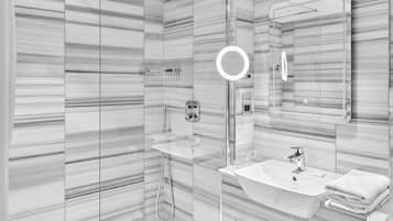 Un baño moderno con cabina de ducha de vidrio, tocador con lavabo y un espejo grande.