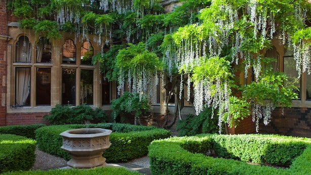 A courtyard with a fountain, trimmed hedges, and hanging white flowers. - Warren House (Kingston Upon Thames)