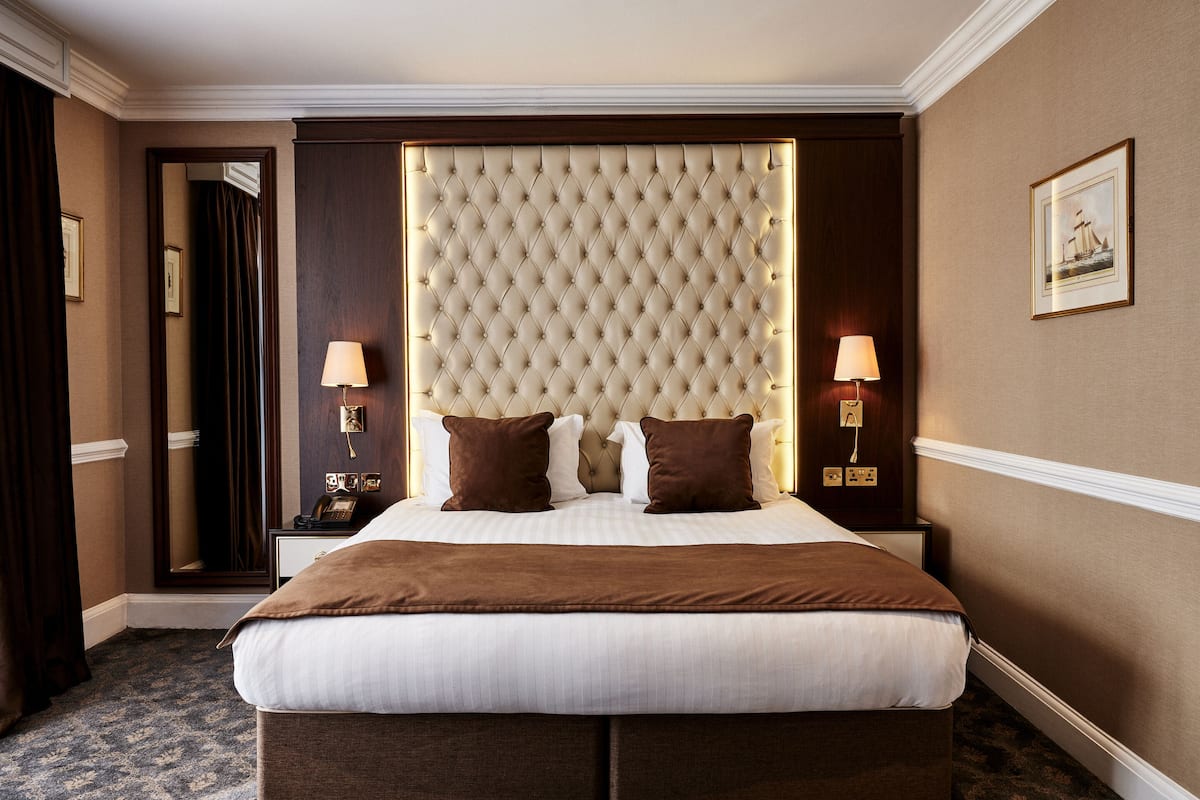 A large bed with a tufted headboard, two bedside lamps, and a framed picture on the wall.