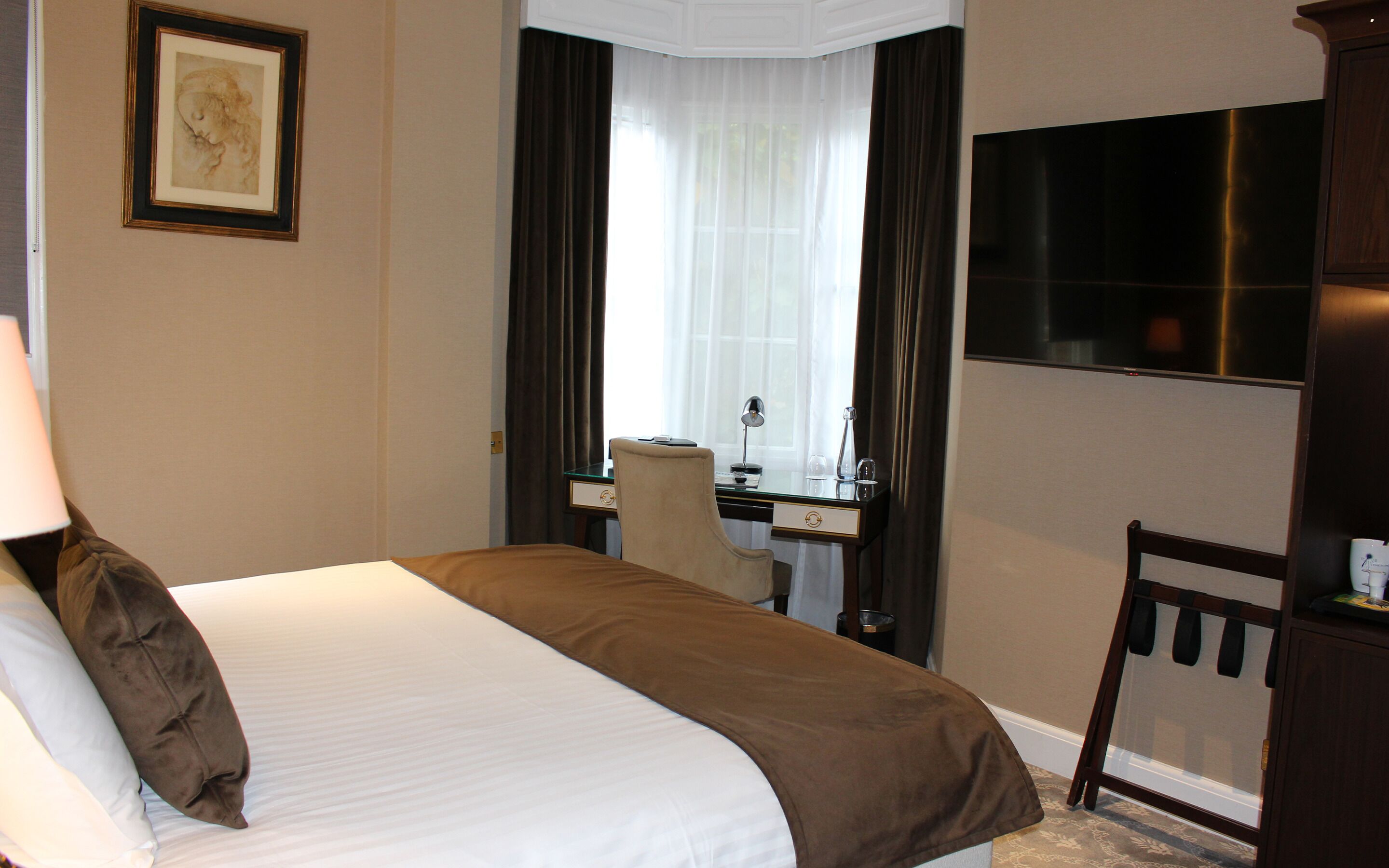 Ein Hotelzimmer mit Bett, Schreibtisch, Stuhl, Fernseher und einem Fenster mit Vorhängen.