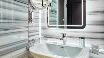 A modern bathroom with a marble backsplash, a large sink, a mirror with a light, and toiletries on the counter.