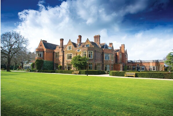 A large, historic brick building with multiple chimneys and large windows, surrounded by a well-maintained lawn and a few benches. - Warren House (Kingston Upon Thames)
