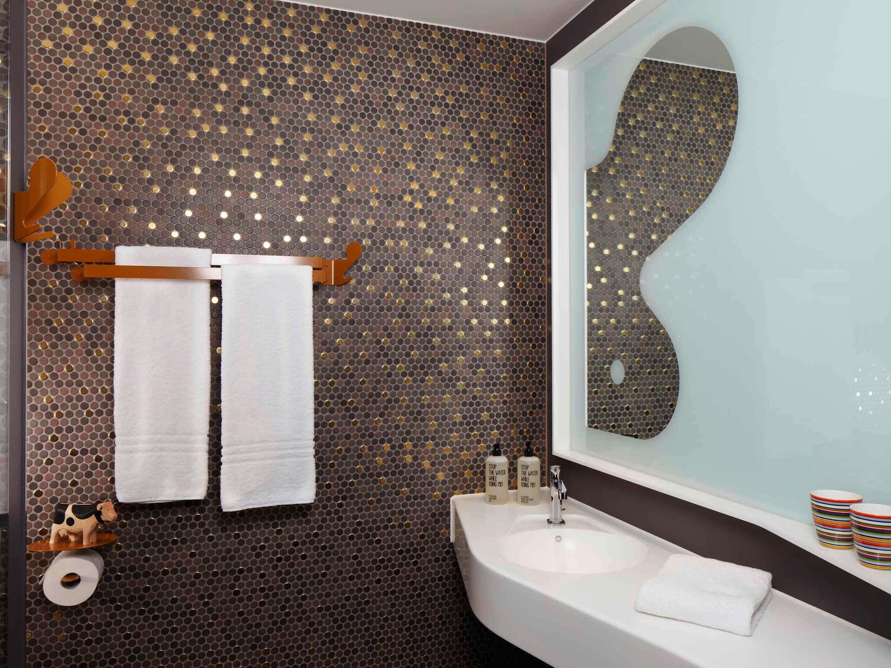 A bathroom with a large mirror, a sink, two towels, a toilet paper roll, and a soap dispenser.