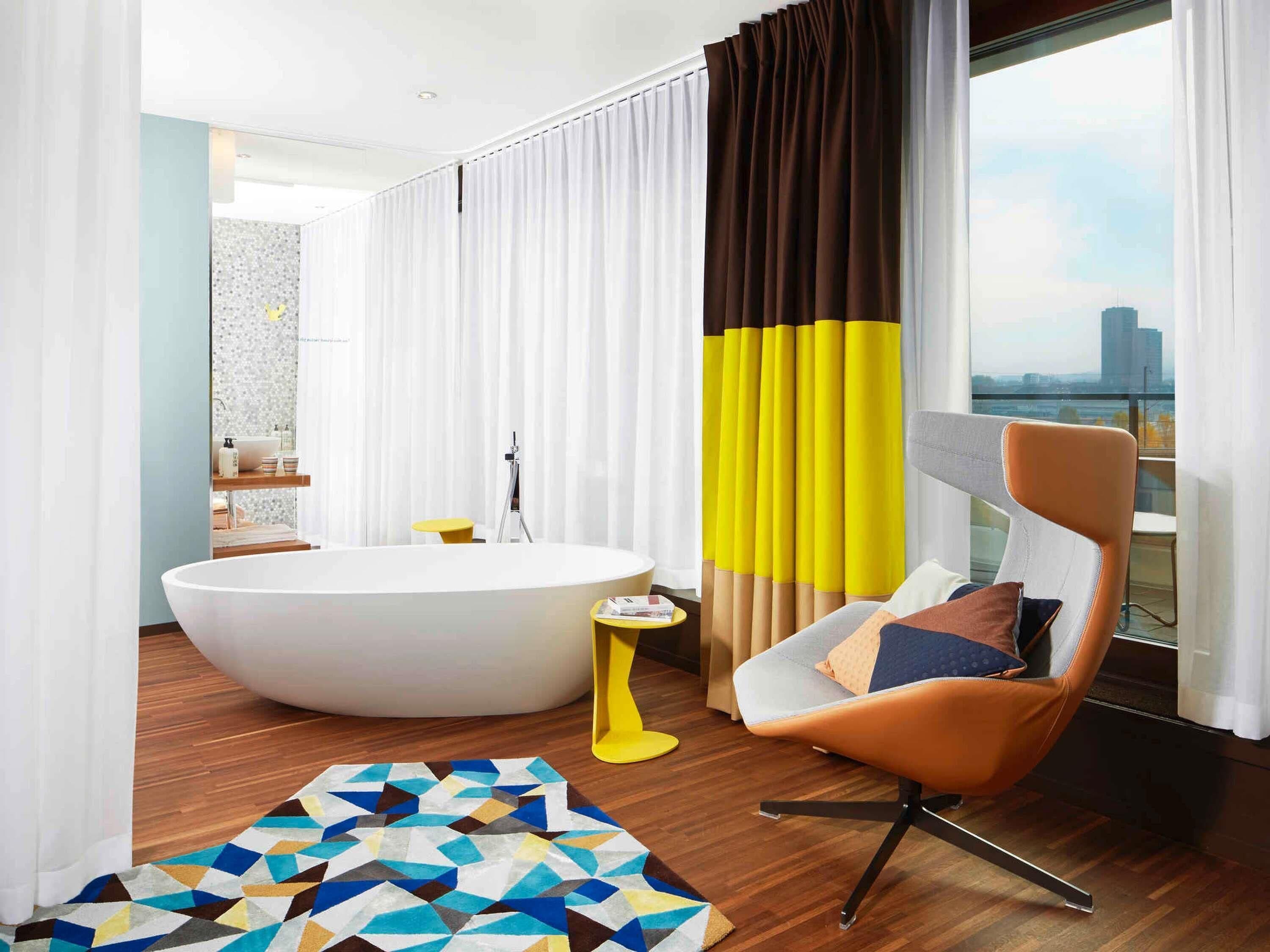 A modern bathroom with a freestanding bathtub, a yellow side table, and a geometric-patterned rug.