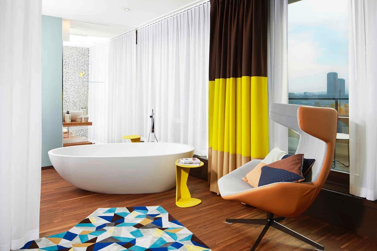 A modern bathroom with a freestanding bathtub, a yellow side table, and a geometric-patterned rug.