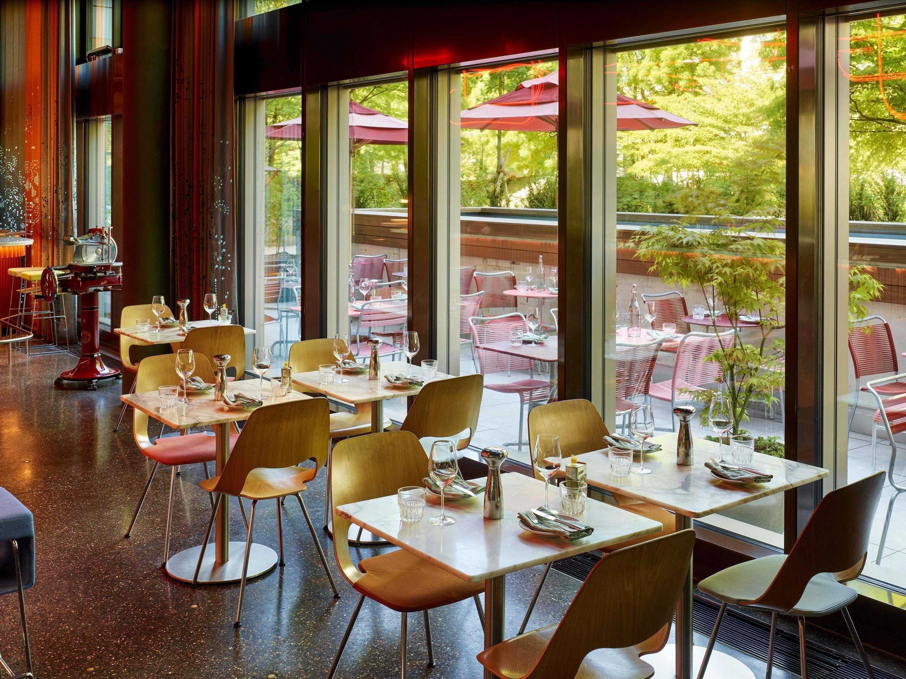 Un espace de restauration intérieur avec des tables et des chaises, de grandes fenêtres et une vue sur l’espace extérieur aménagé pour les repas.