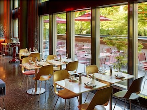An indoor dining area with tables and chairs, large windows, and a view of the outdoor seating area. - 25hours Hotel Zurich West (Zürich)