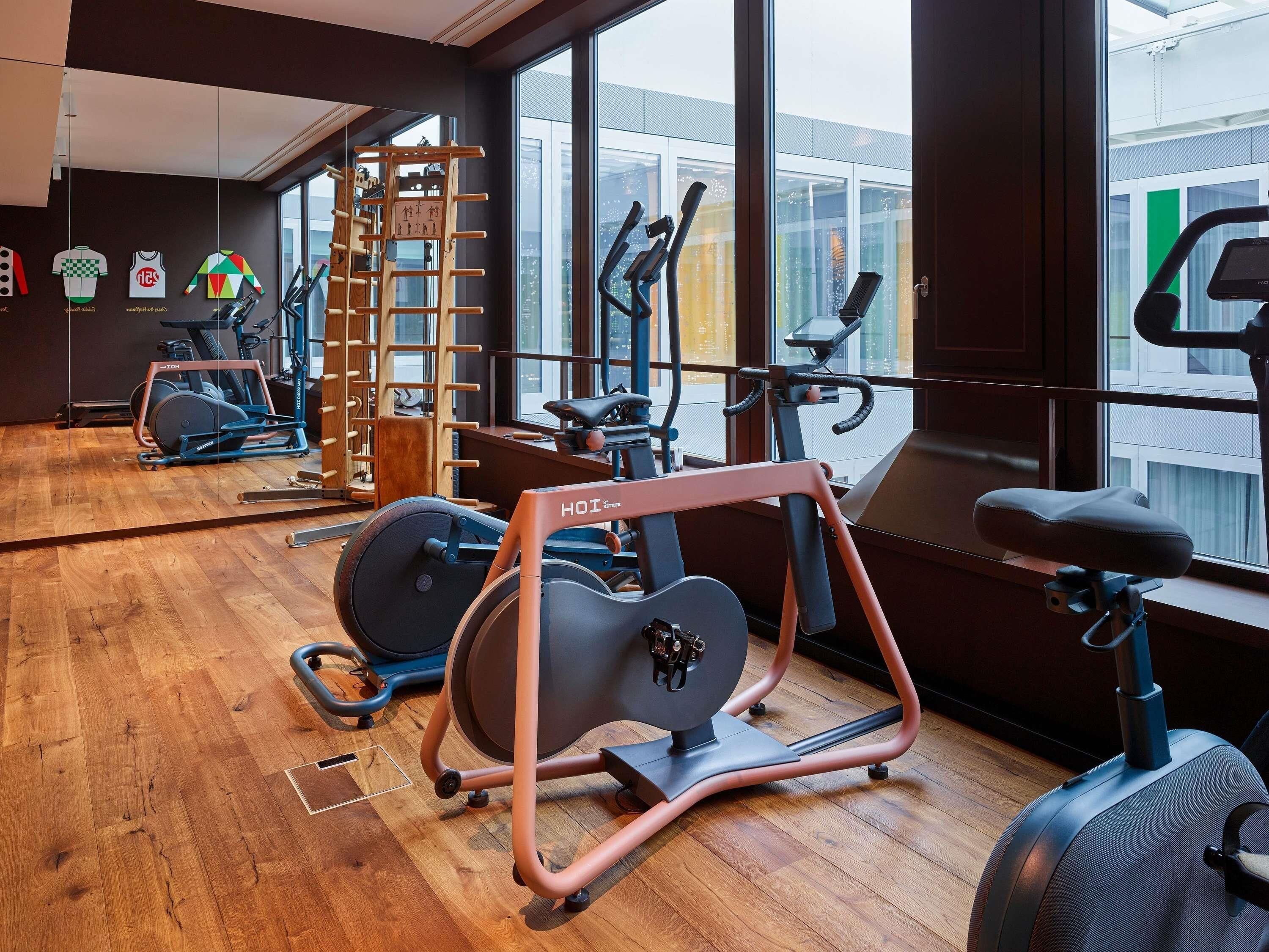 A gym with exercise equipment, large windows, and a wooden floor.