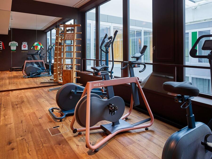 A gym with exercise equipment, large windows, and a wooden floor.