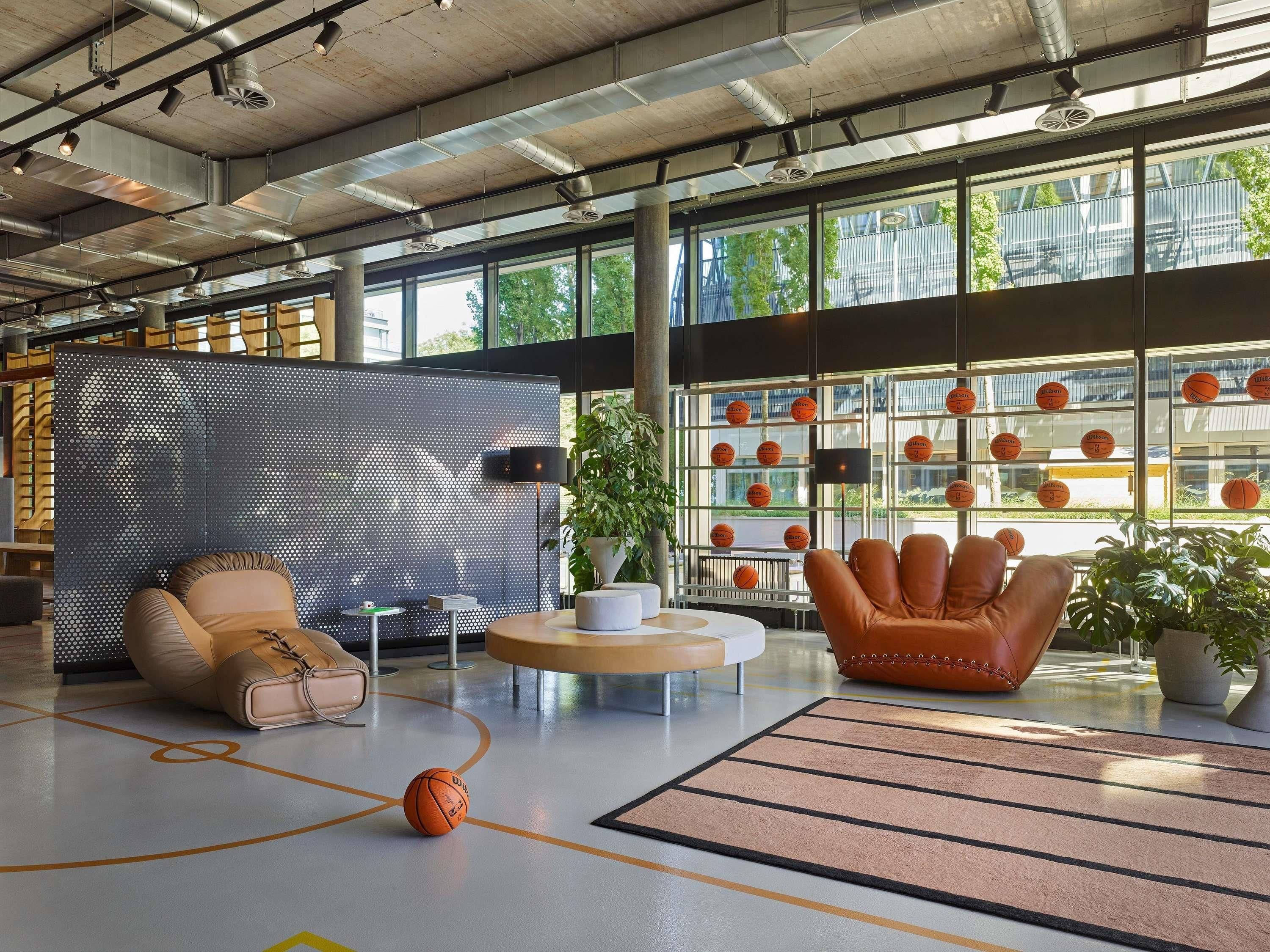 A spacious indoor area with a basketball court, seating areas, and a wall with basketballs.