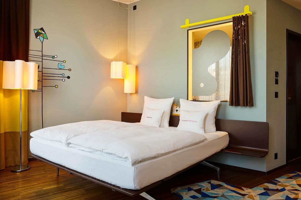 A hotel room with a bed, bedside lamps, a mirror, and a geometric-patterned rug.